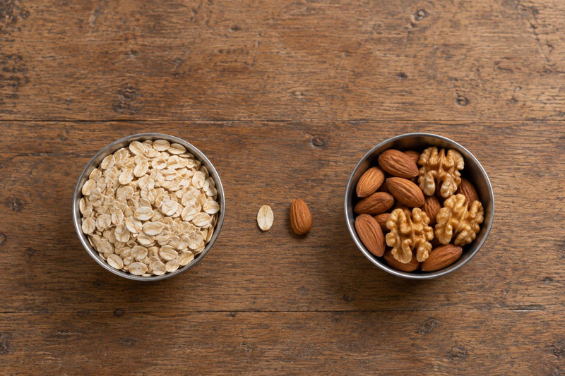 Rolled oats in one steel bowl next to almonds and walnuts in another, showing that oats are a grain and not a nut